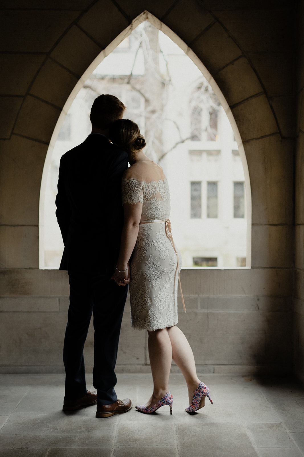 Just Married photo session couple in an old Chicago church Chicago church cloister moody photo, bride rests her head on grooms shoulder, photo from behind with beautiful light