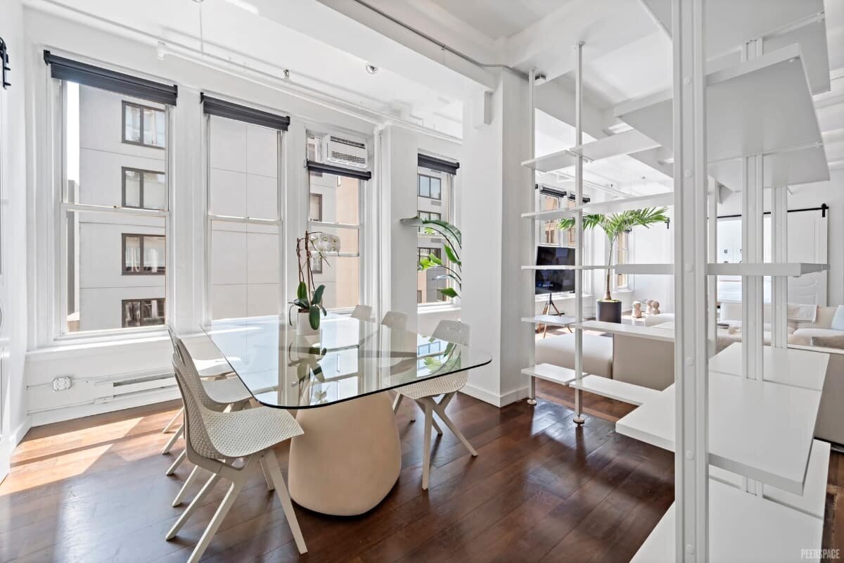 NYC brand photography studio dining area with glass table, white chairs, and large windows.