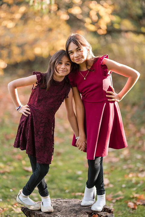 A family of four, dressed in fall colors, together in vibrant foliage of Lincoln Park in West Seattle. The sun filters through the trees at golden hour.  Casting a warm glow on the family. . This photo is a perfect example of fall family mini sessions with Heleyna Holmes Photography,