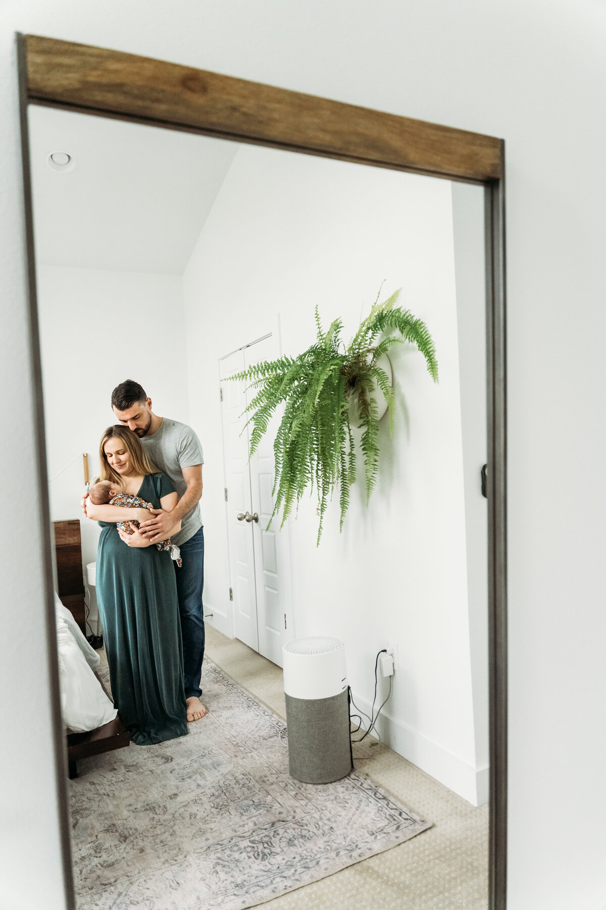 Newborn Photographer. in a large mirror a mother, father and baby being held are reflected