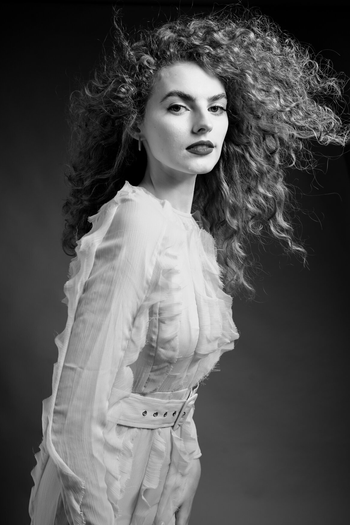 a woman with curly hair posing to the camera while the air if lying her hair away