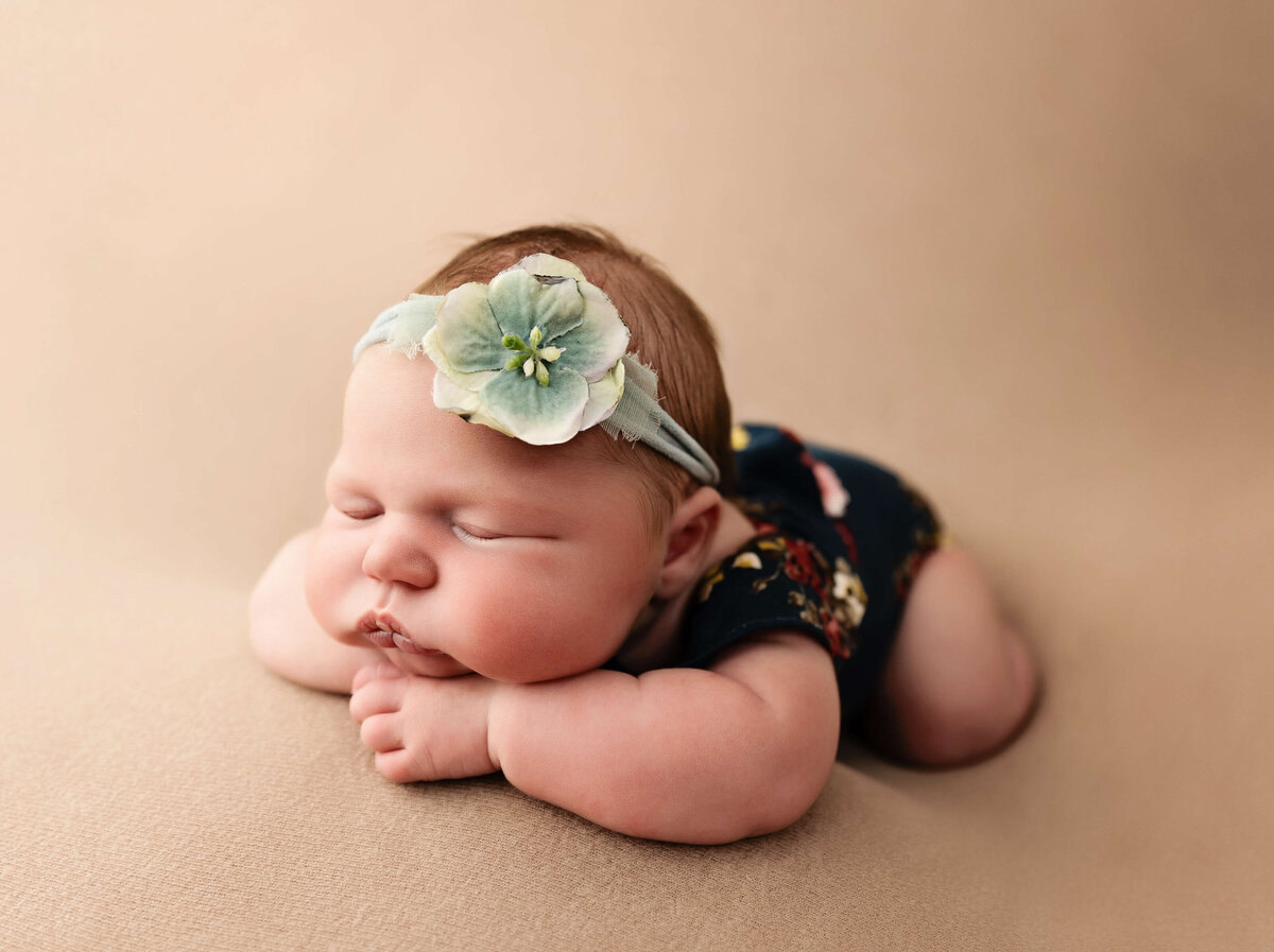 Newborn baby girl in chin on hands pose in a teal flowered romper in a photography studio in Erie Pa