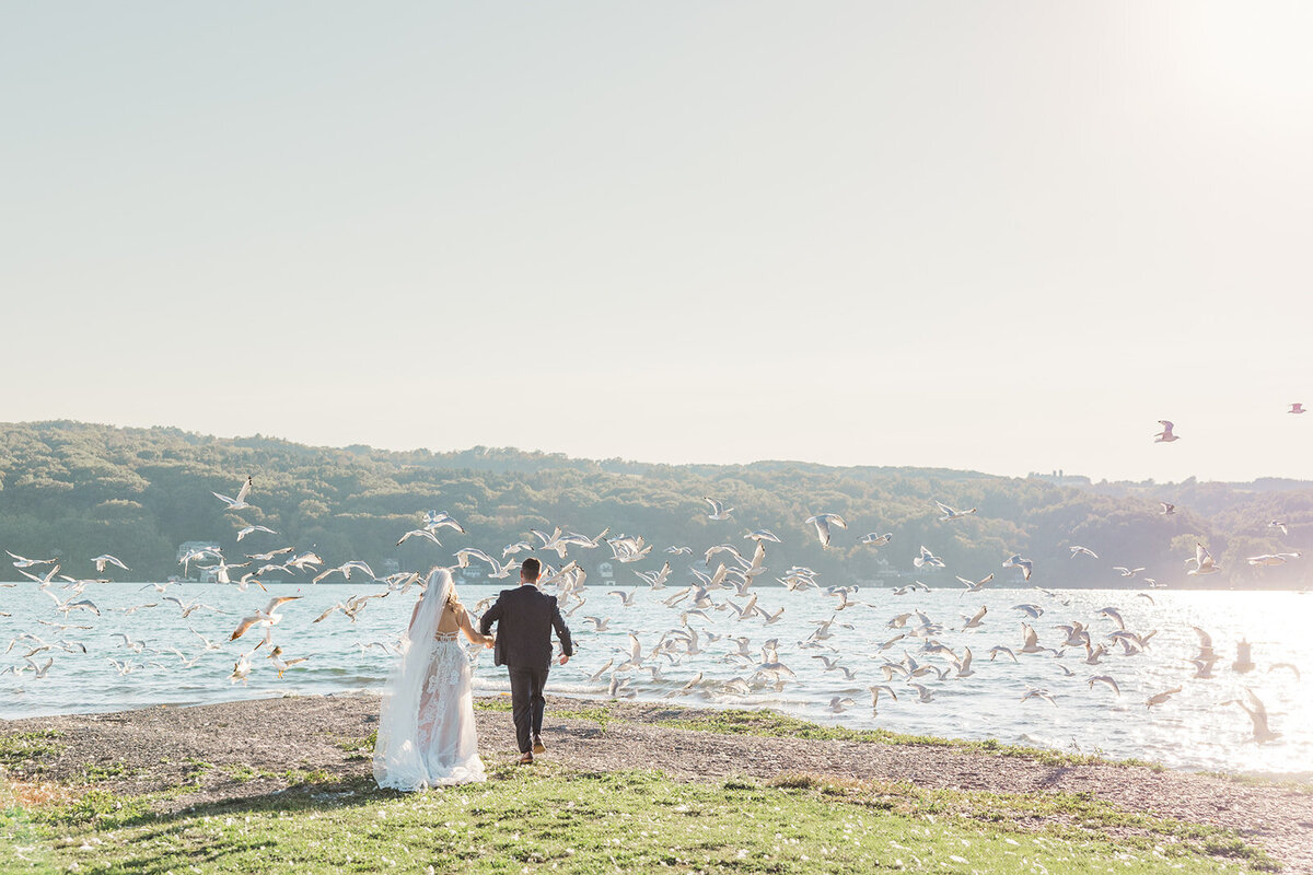 Bride and groom walking towards ocean with seagulls flying overhead, Finger Lakes wedding, NY