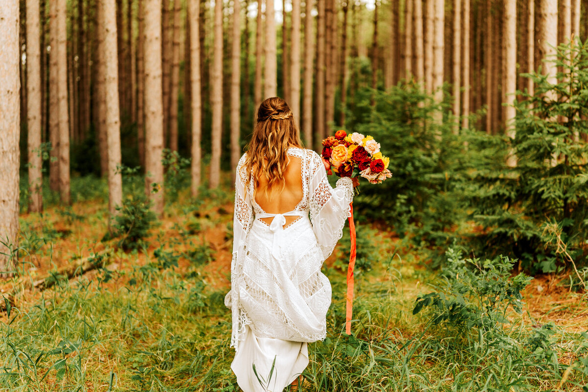 boho bride walking through forest with flowers
