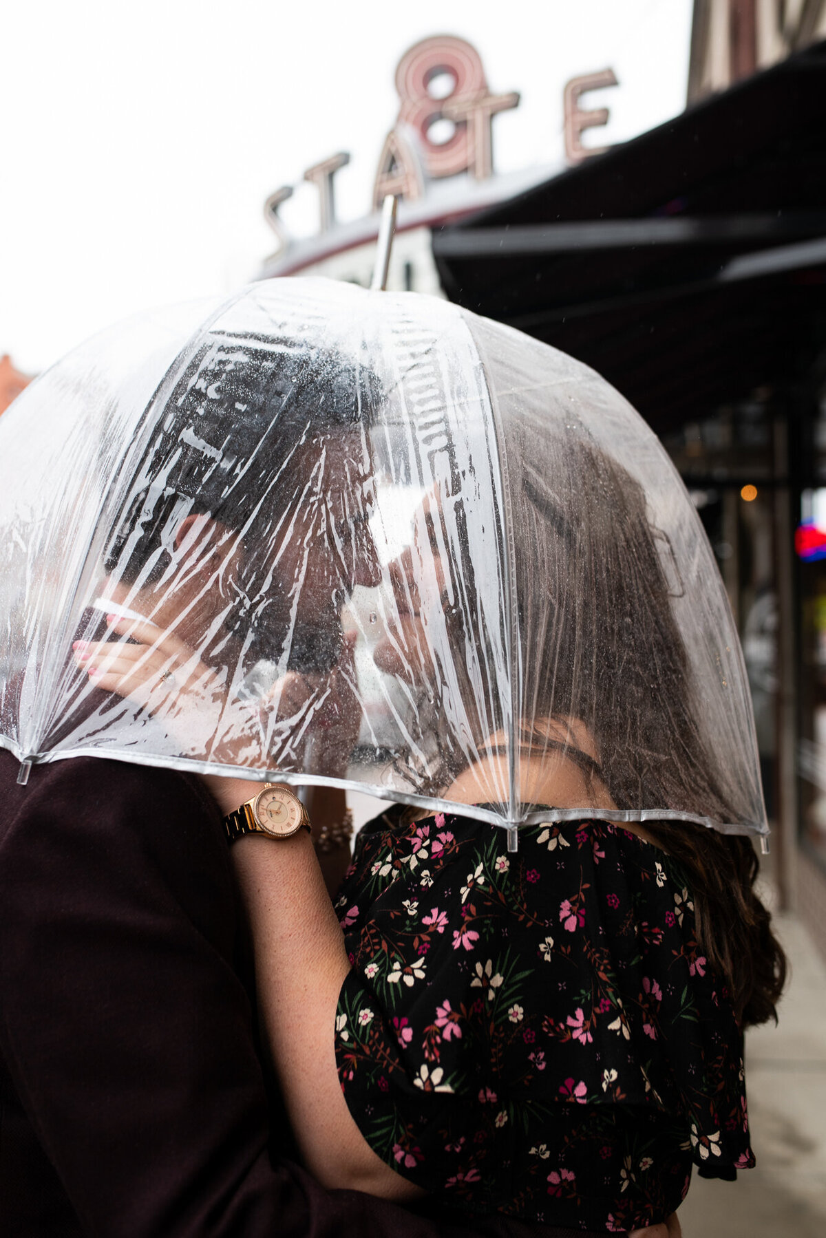 Couple share kiss under umbrella during rainy day engagement session