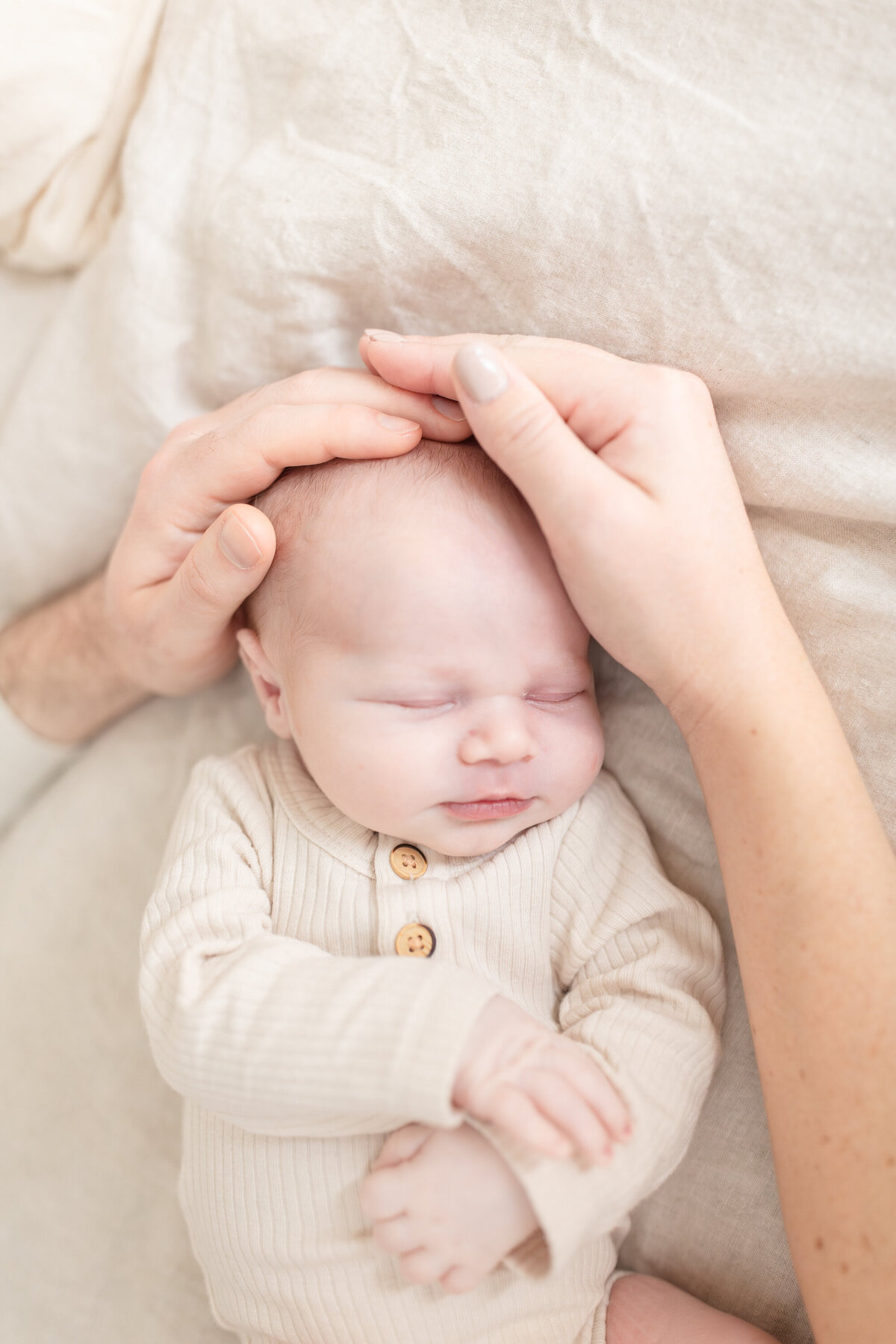 Close-up image of a newborn with tiny hands gently cradled by mom and dad’s hands. The intimate moment captures the love, protection, and connection of the new family