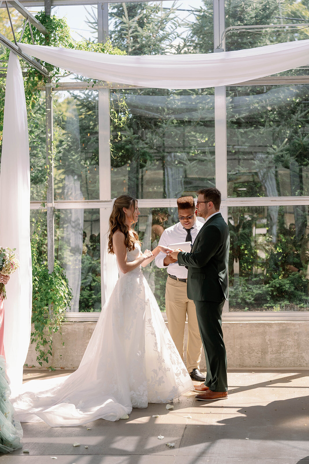 Wide shot of the bride and groom exchanging rings during their Ivy House greenhouse ceremony in Saugatuck, Michigan.