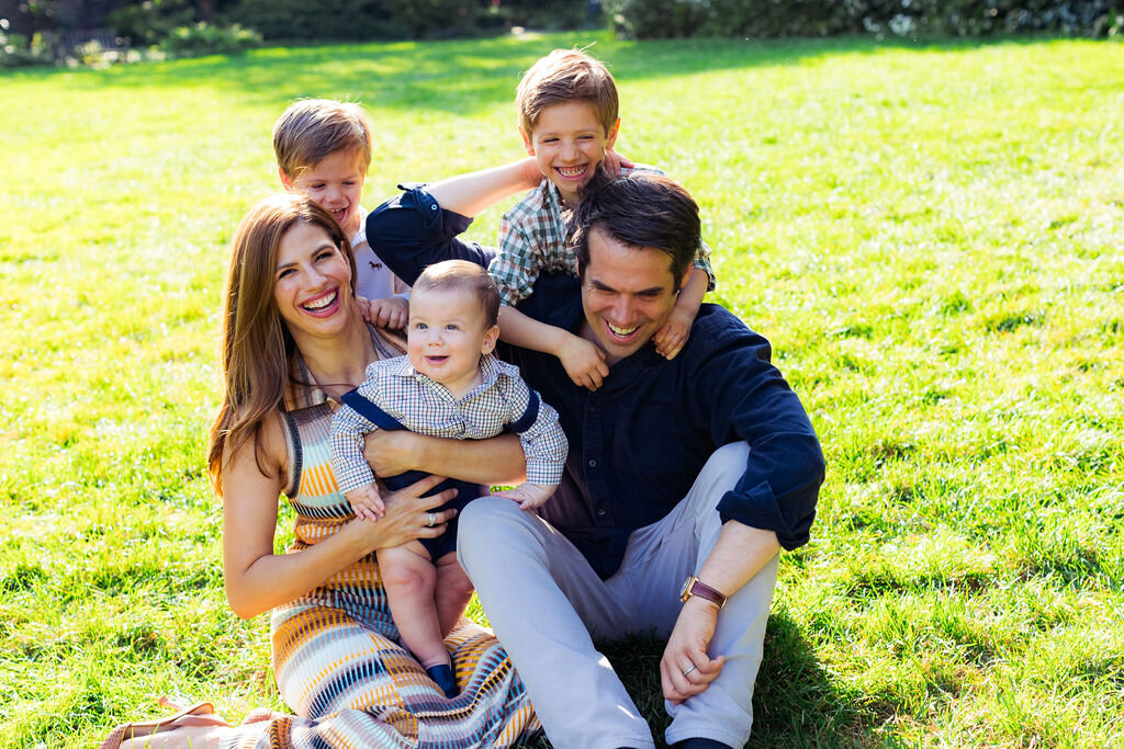 A family of five laughs while sitting on grass.