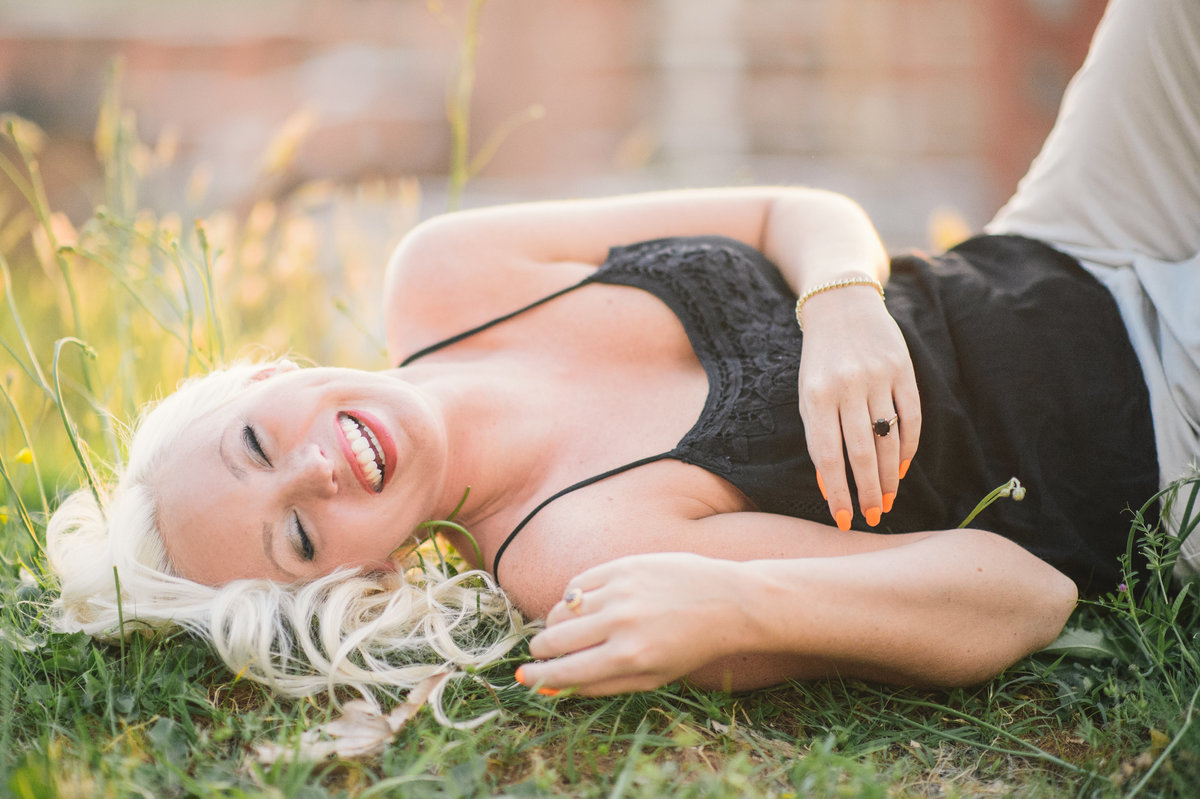 Blonde girl laughing as she lies in the green grass.