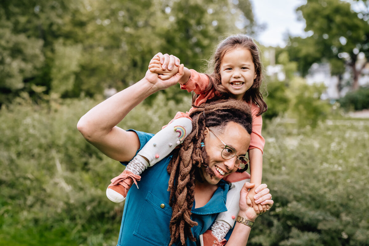 A child is on top of a dad's shoulders, laughing.