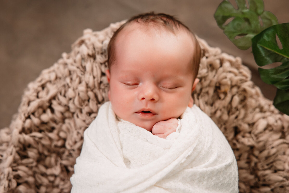 A sleeping newborn baby sleeps in a white onesie with mouth open