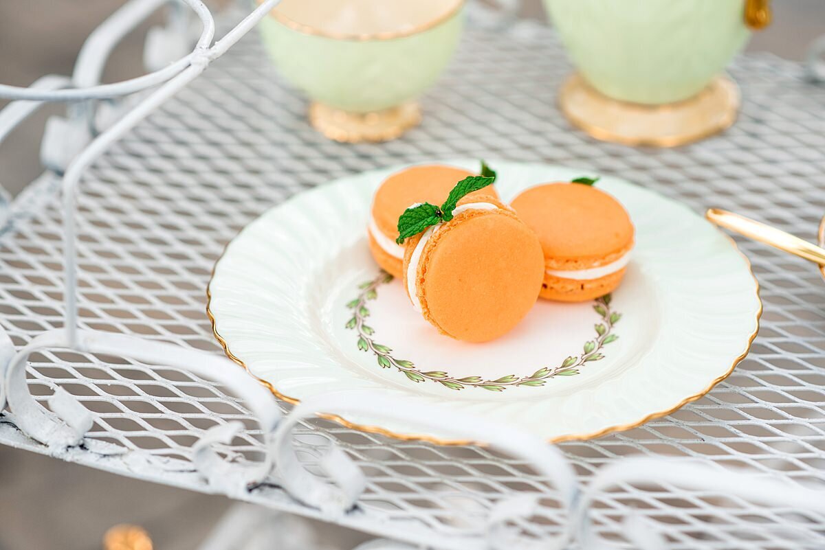 Peach macarons garnished with mint leaves on a white vintage china plate with gold accents on a metal dessert cart