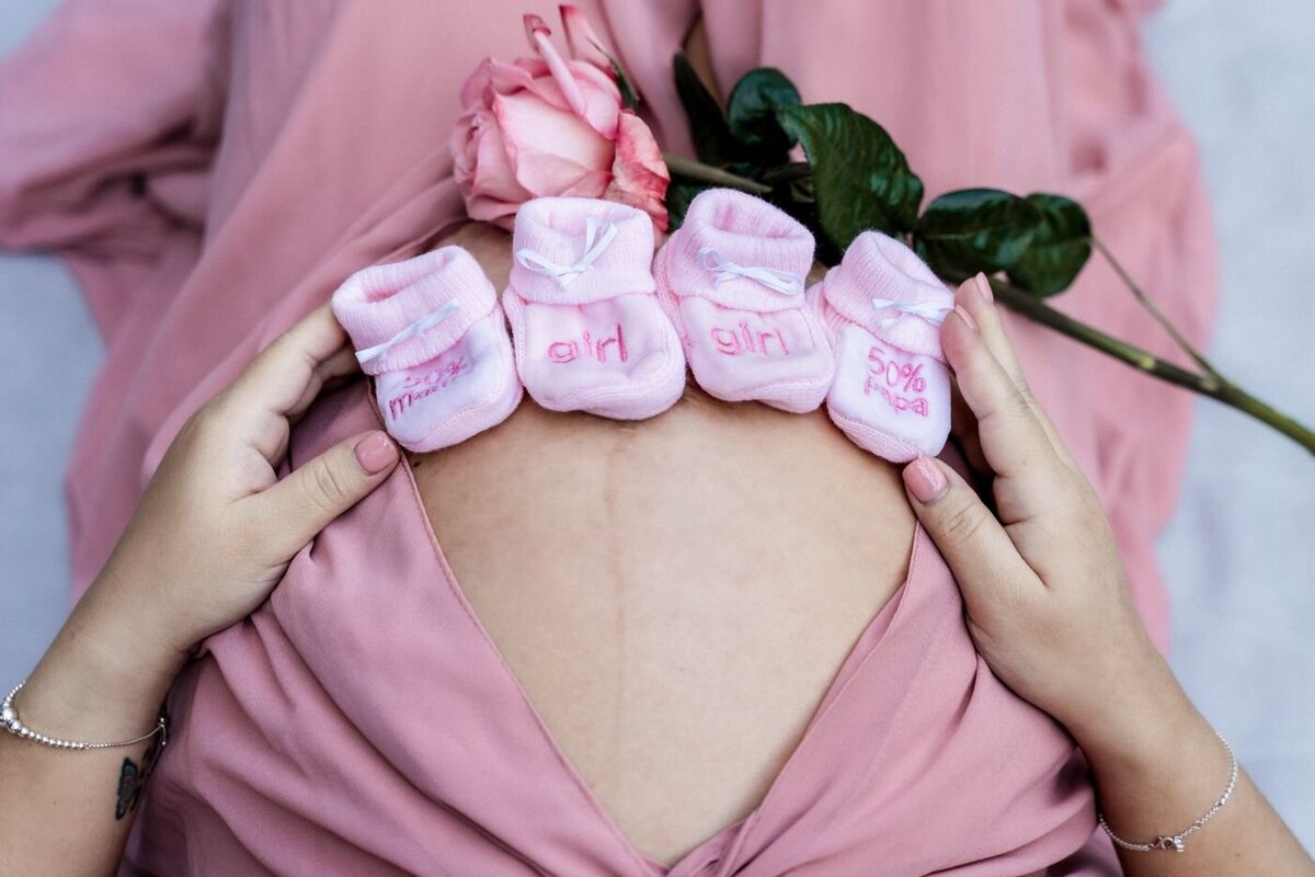 Close-up of pink baby socks arranged on a mother’s belly with a single pink rose.