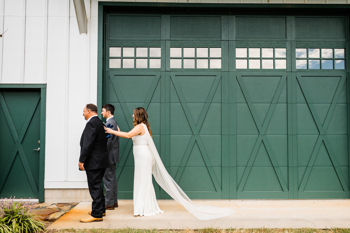 Virginia wedding photographer captures a first look between bride and her father and brother outside of her shenandoah wedding venues reception space with tall green barn doors on a white barn