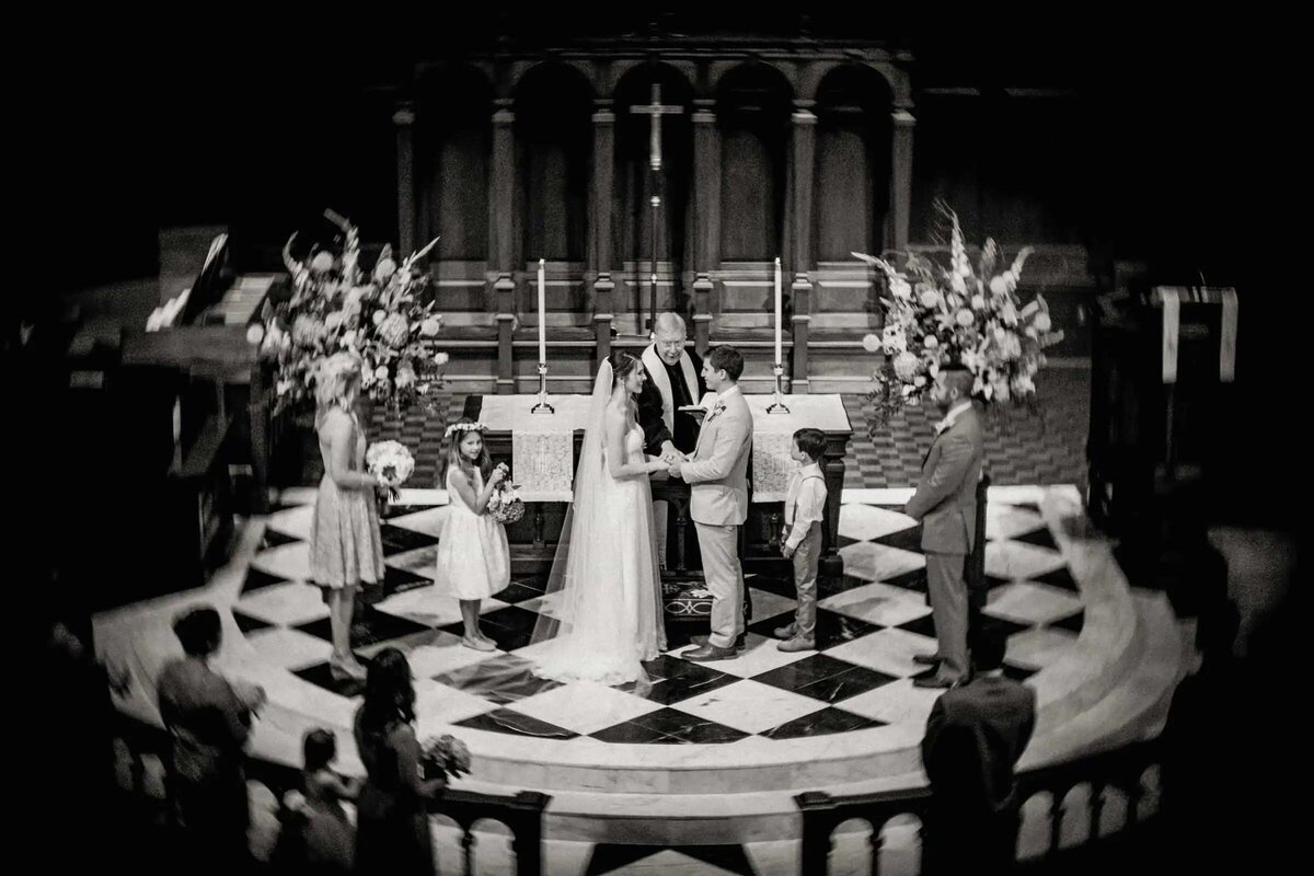A bride and groom stand at the altar in an elegant, softly lit church