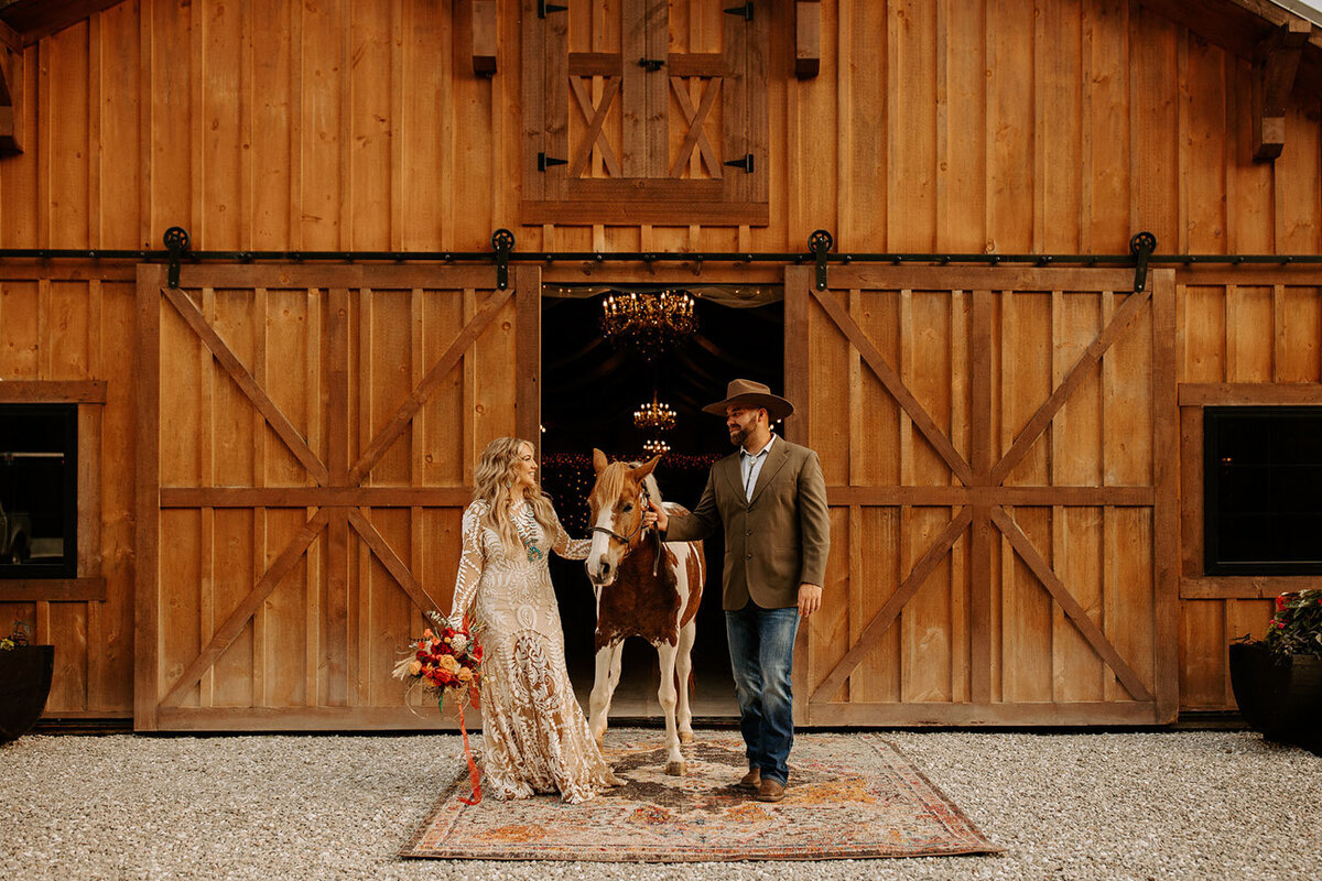 Bride and groom walking a horse in front of a rustic barn venue