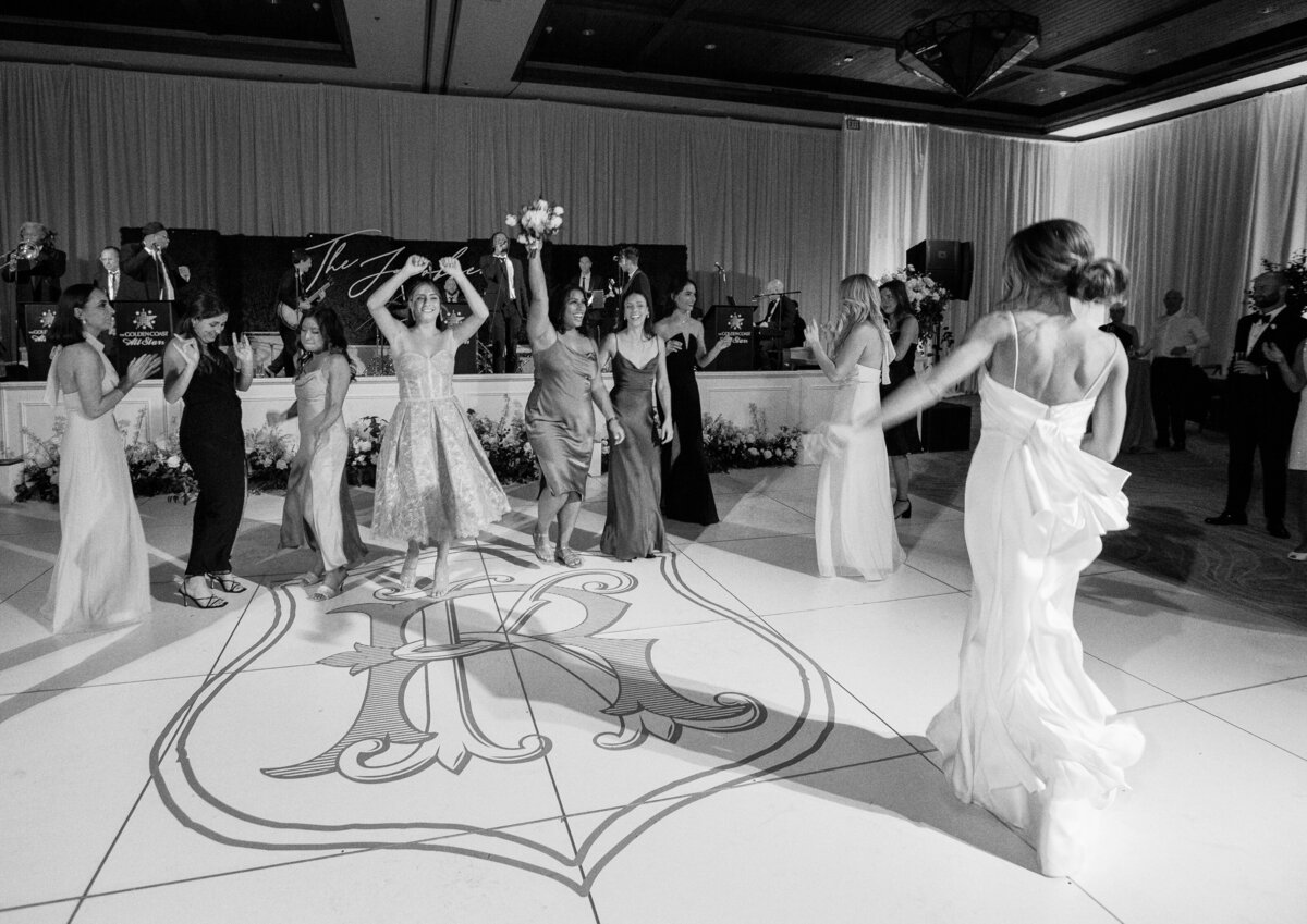 The bride gracefully tosses her bouquet to excited guests on the dance floor, a classic wedding tradition captured beautifully.