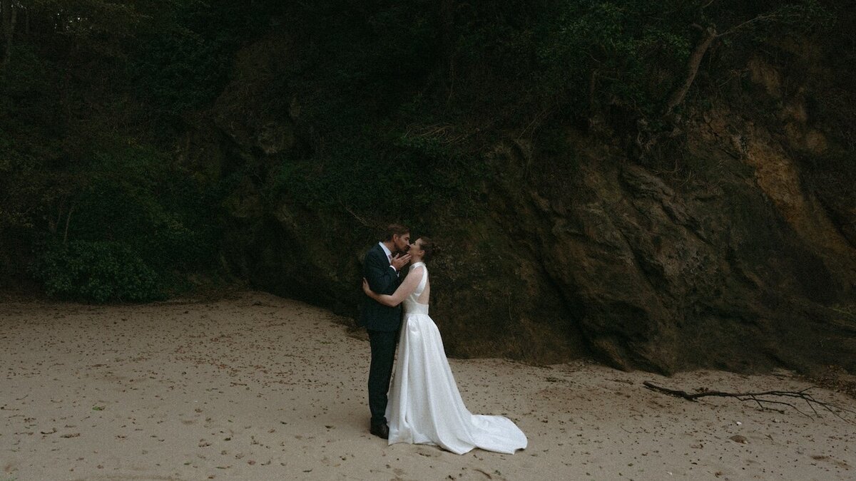 Les mariés échangent un baiser sur une plage, entourée par les falaises verdoyantes. Une scène intime et naturelle, capturée par Kamescop.