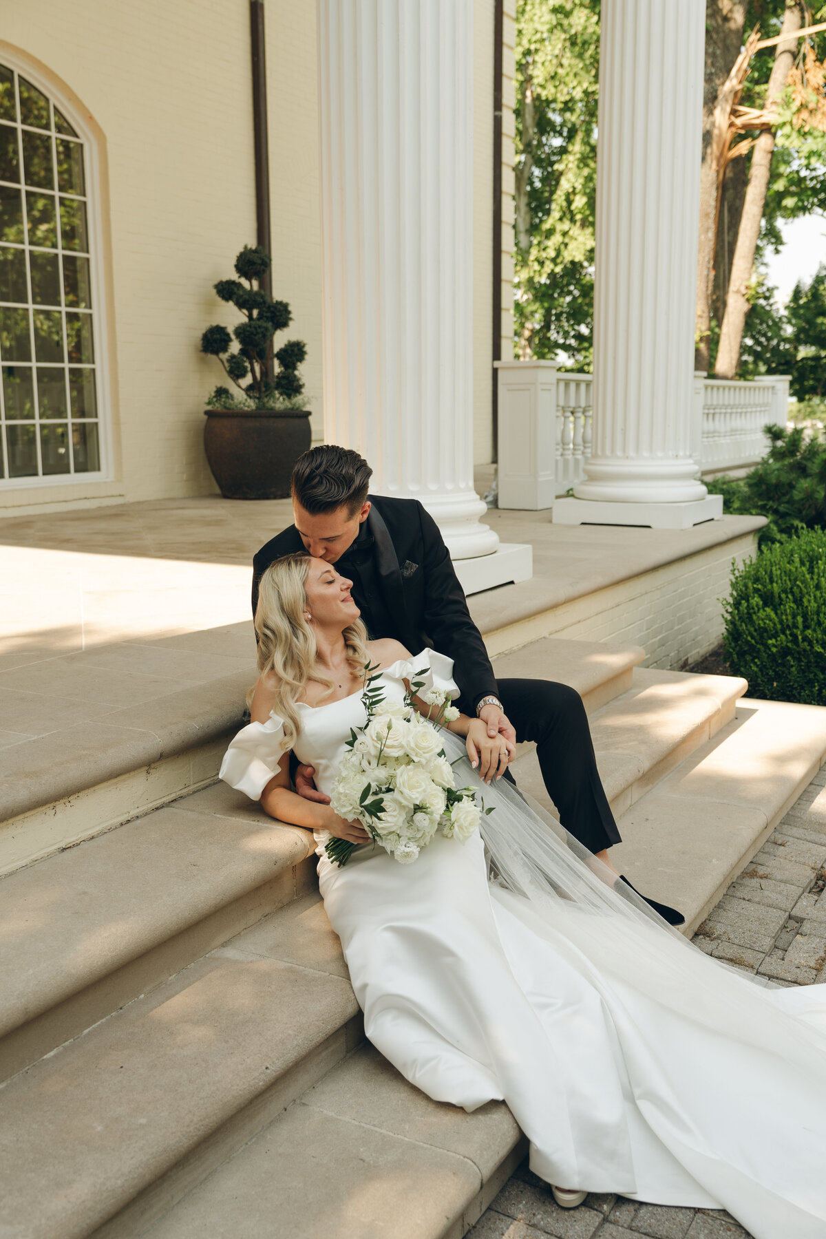 A blonde haired bride sits on the steps with her brown haired groom outside a wedding venue in Nashville Tennessee. 