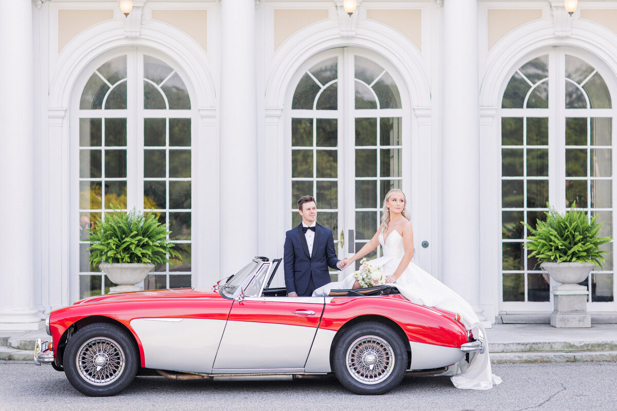 Bride and groom posing with a red vintage car representing editorial Boston wedding photography
