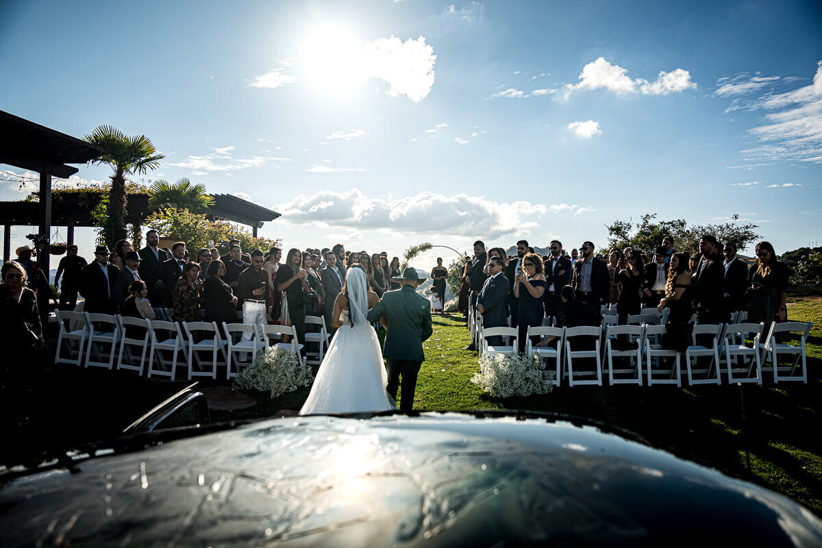 A heartfelt moment as the bride walks down the aisle with her grandfather at Airola Road Vineyard, with a classic car in front and breathtaking views of the Sierra Nevada foothills in the background.