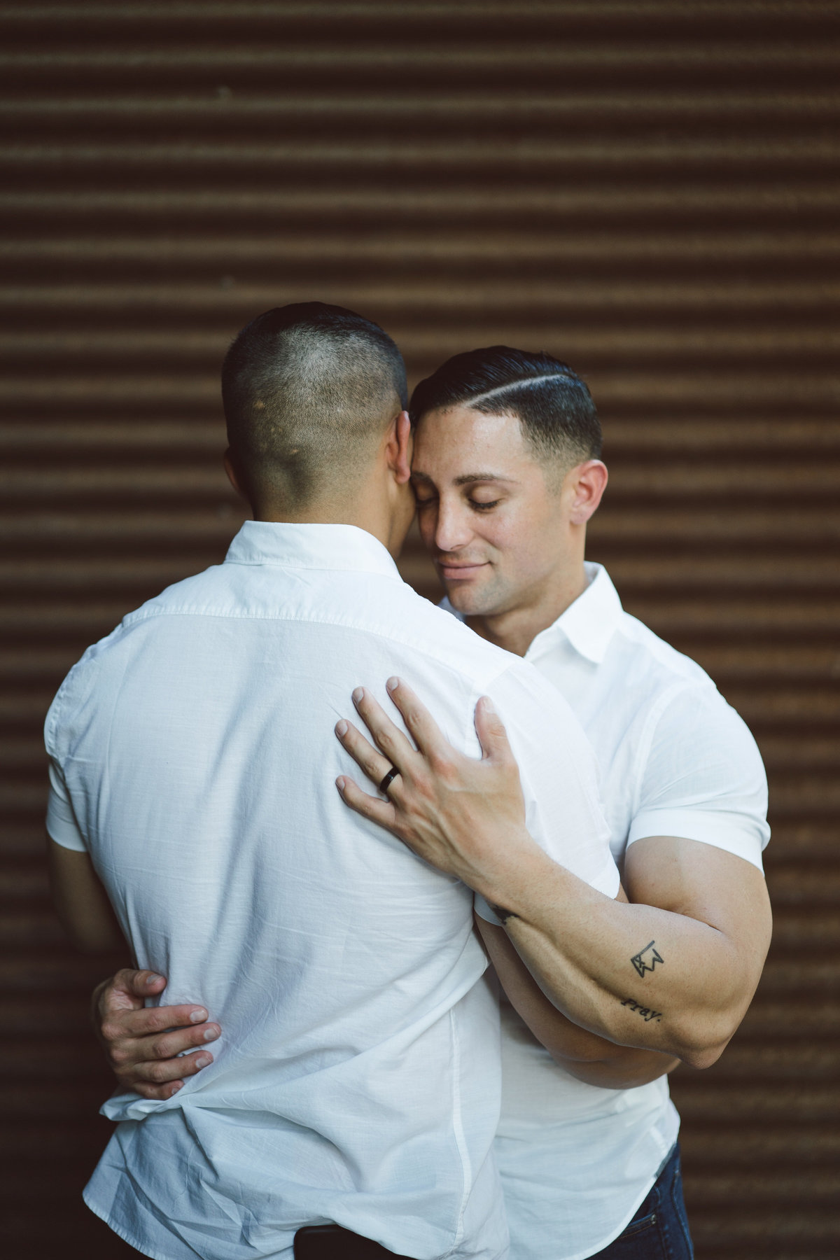 Engaged couple, two men embracing each other with eyes closed at the Historic Pearl. Same sex engagement session.