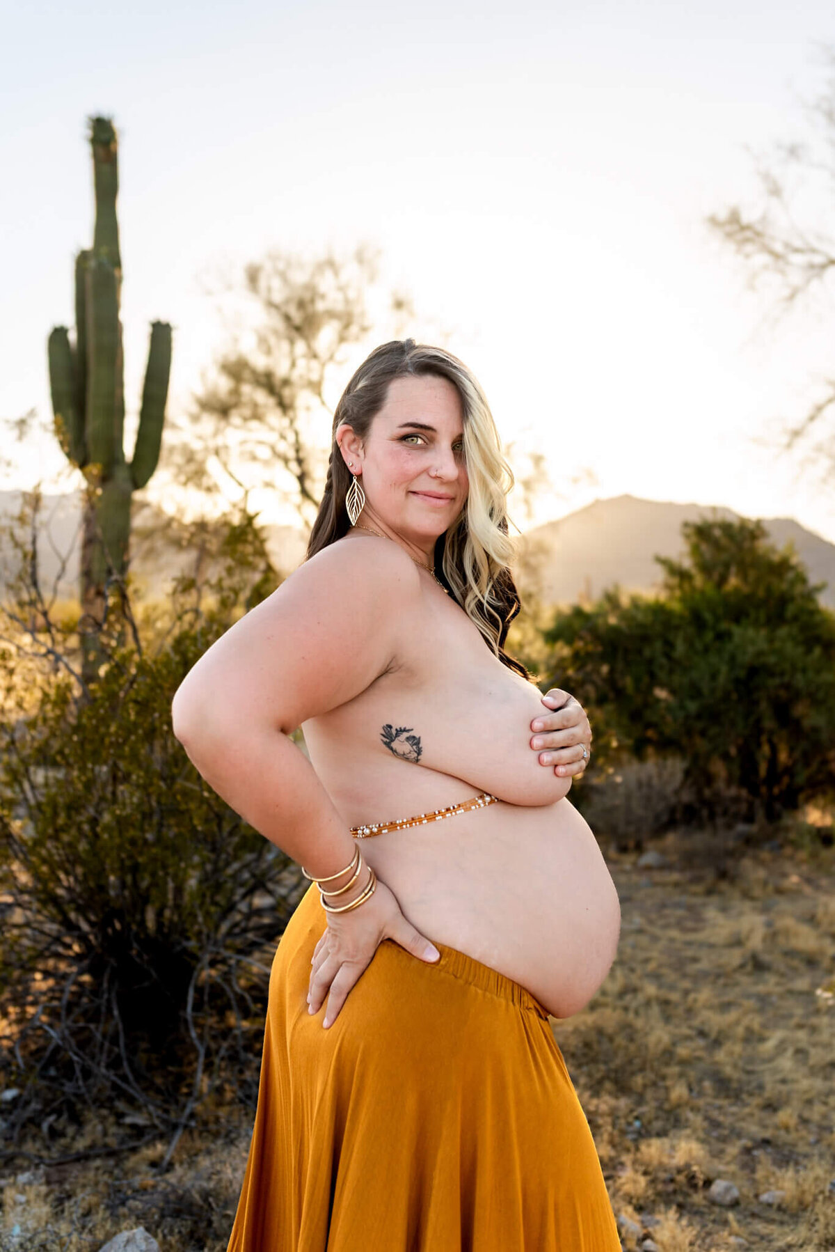 Intimate portrait of expecting mom showing skin of her belly and covering breast in Arizona desert