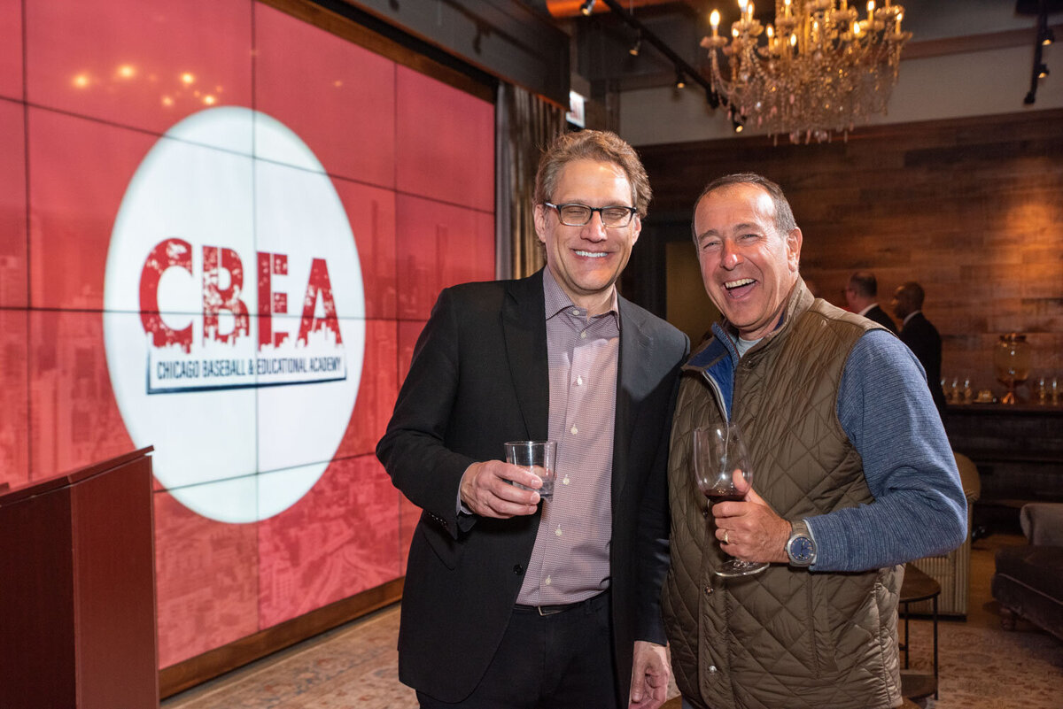 Two men smiling at a social event in front of a CBEA sign.