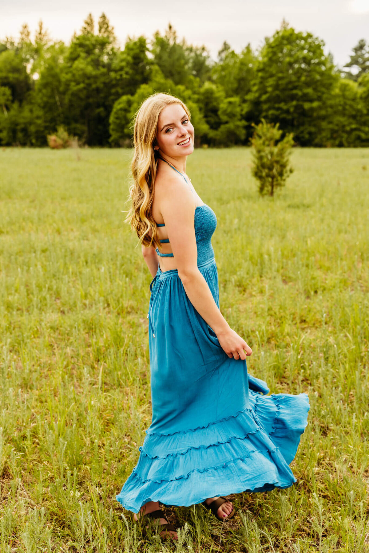blonde senior girl spinning in a maxi blue dress in a field by Ashley Kalbus Photography