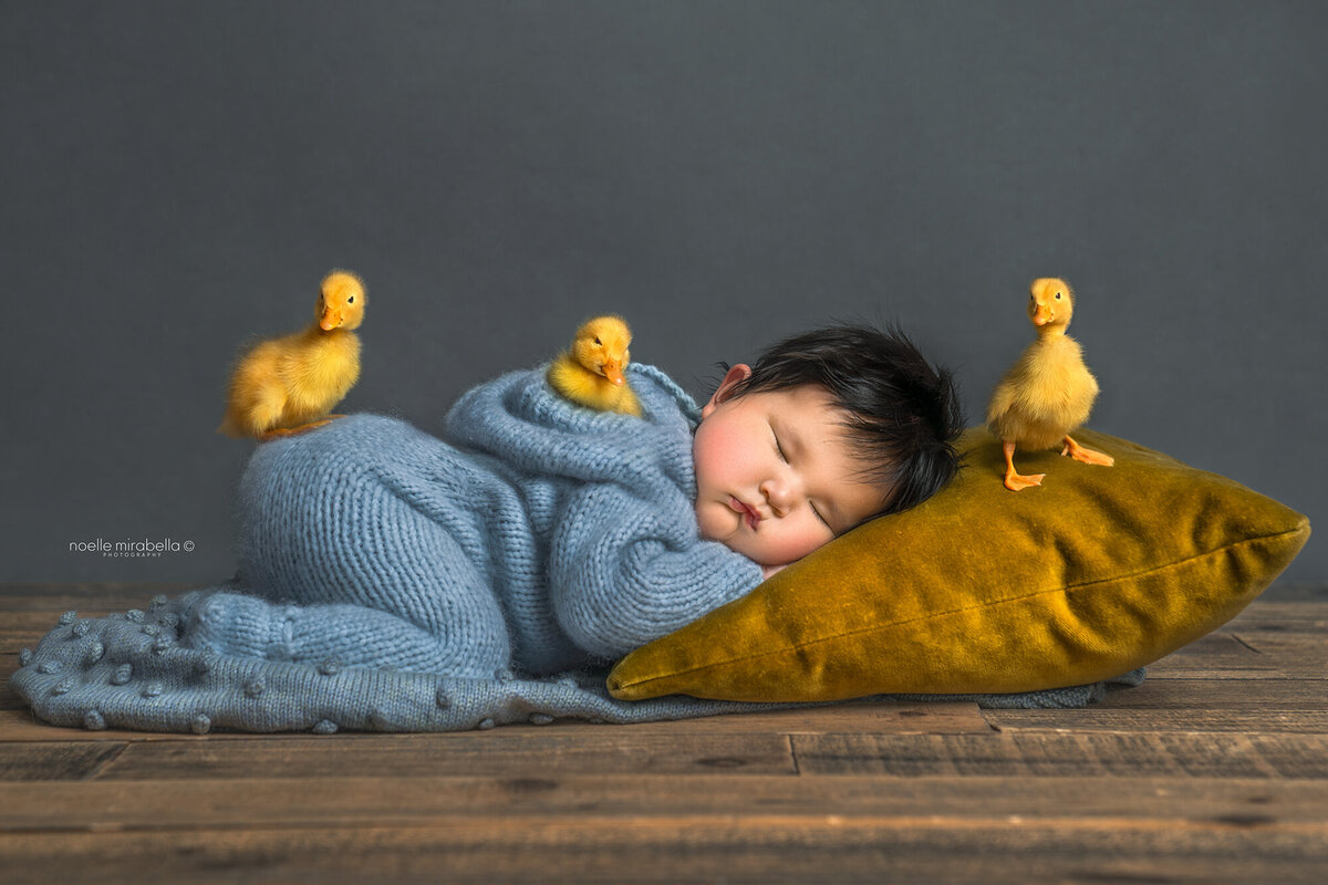 Baby sleeping on the floor with little ducklings playing on her.