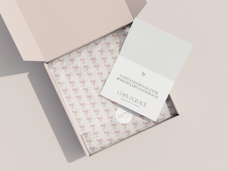 Open Gaby & Grace shipping box featuring custom blush patterned tissue liner and branded insert card with shop information and logo for a premium unboxing experience.