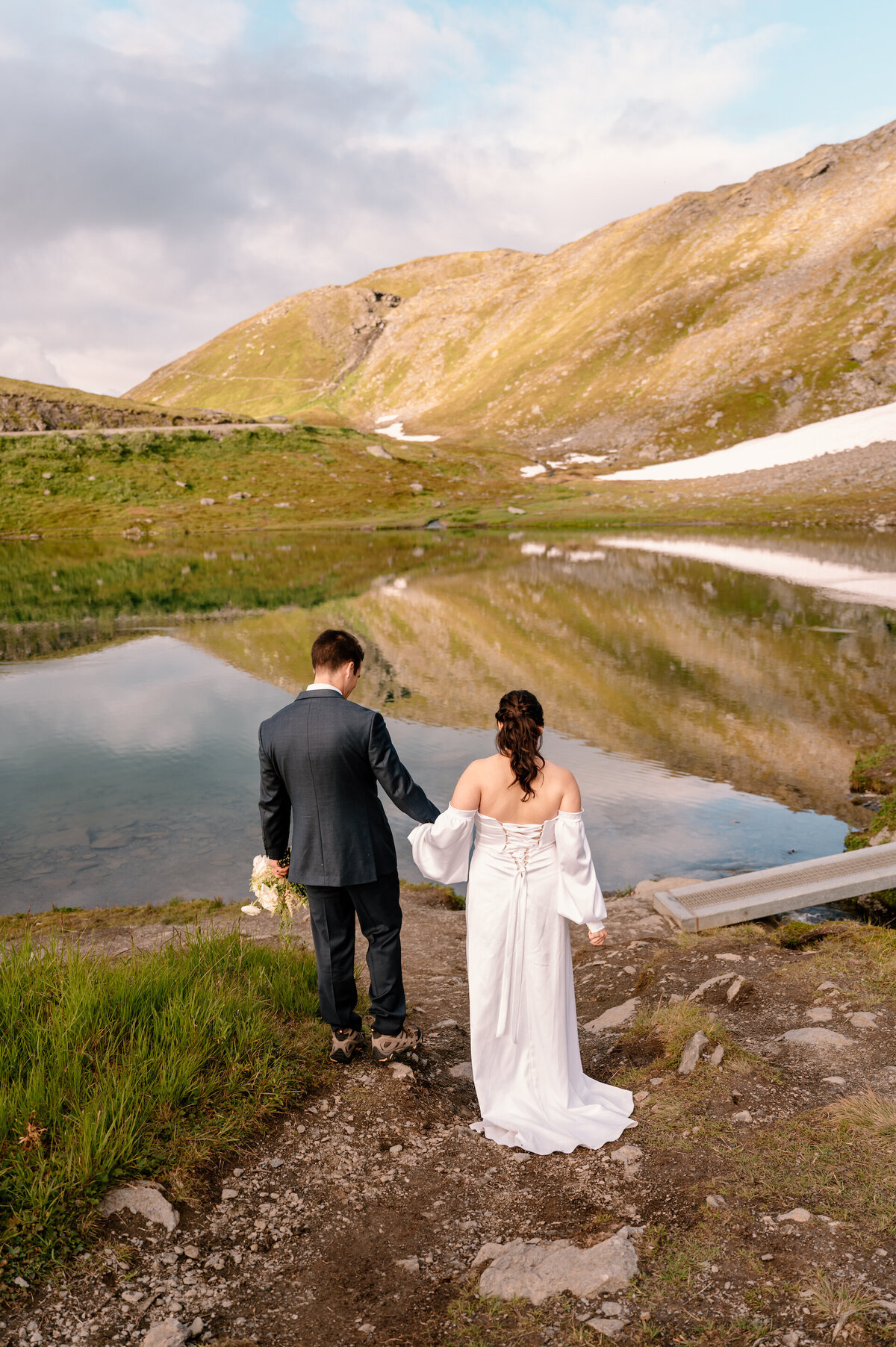 bride and groom walking near a lake in the mountains
