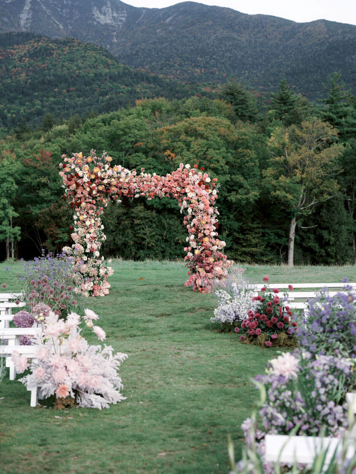 A beautiful wedding arch full of flowers, trees and mountains is in the background at The Ausable Club,NY. Image by Jenny Fu Studio.