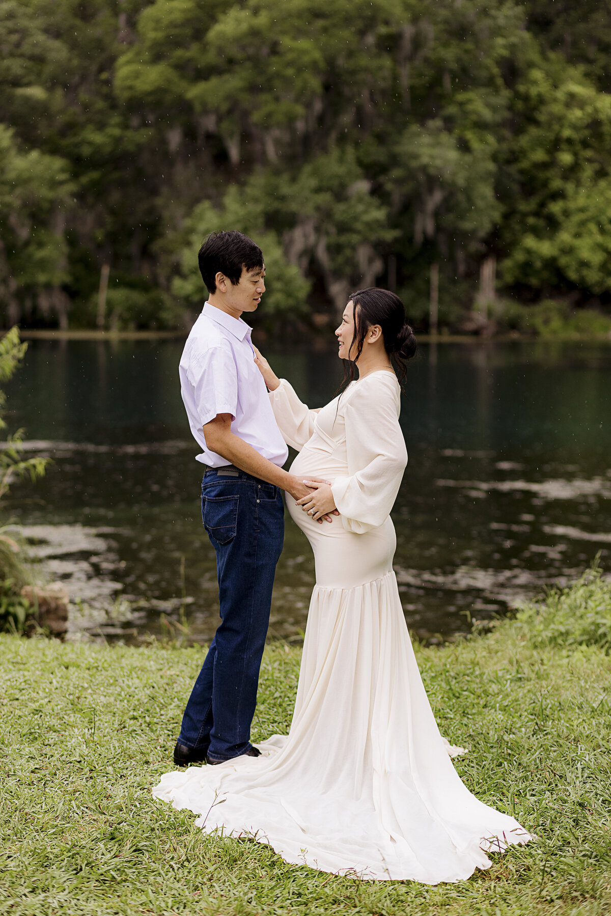 couple facing each other holding pregnant belly outside