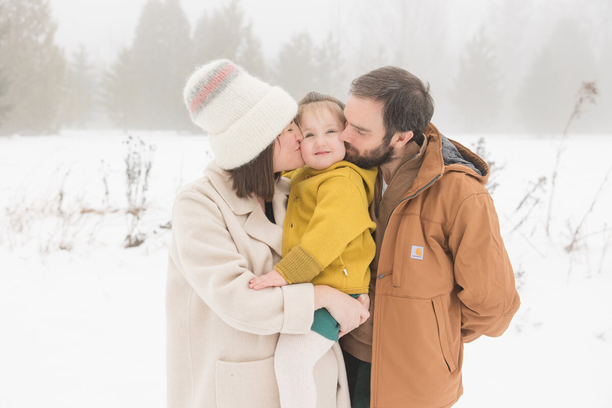 Parents holding their little girl and kissing her on the cheek