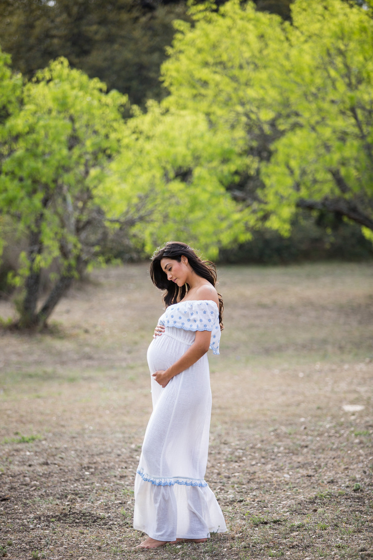 Pregnant mother in see-through maternity white dress standing in field at Denman Estate Park in San Antonio.