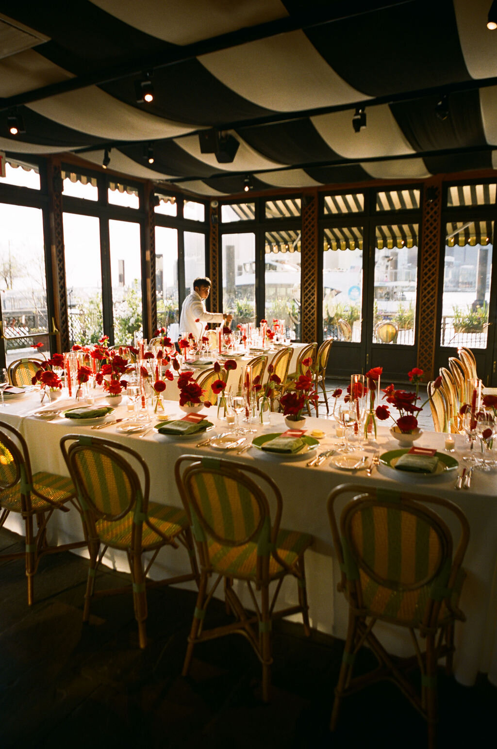 The River Cafe dining room set with long tables, wooden chairs, and red florals