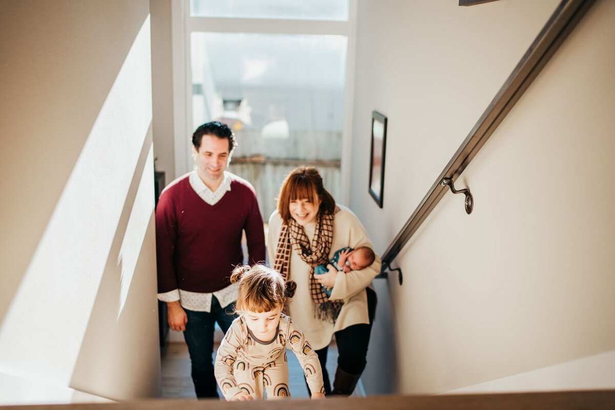family-of-four-walking-on-stairs-holding-their-newborn-girl