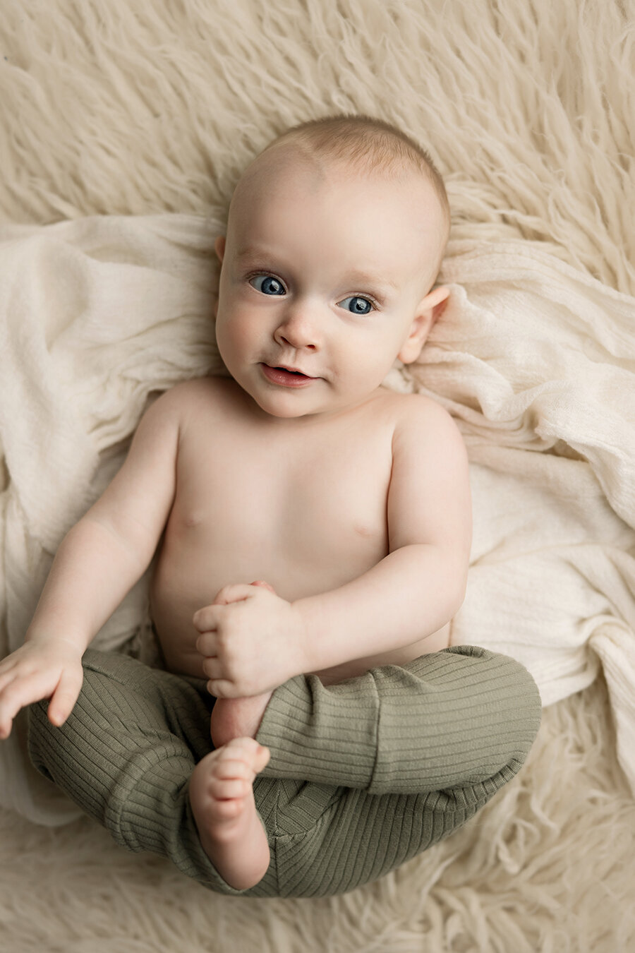 Baby boy in Fort Collins photo studio holding his foot while he lays on a rug