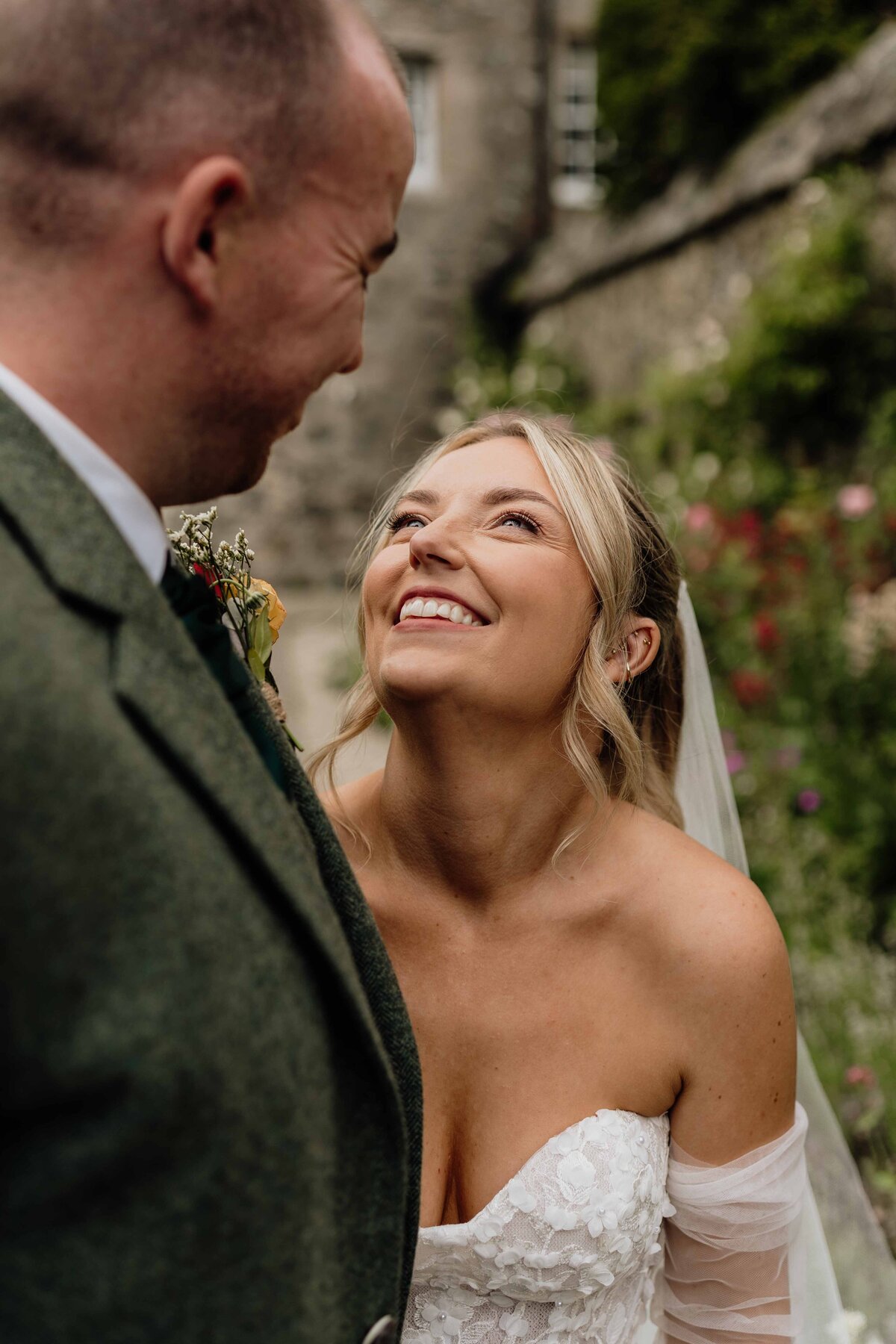 A bride photographed to the side of a groom. She looks lovingly at him in the garden of Barra Castle in Aberdeenshire.