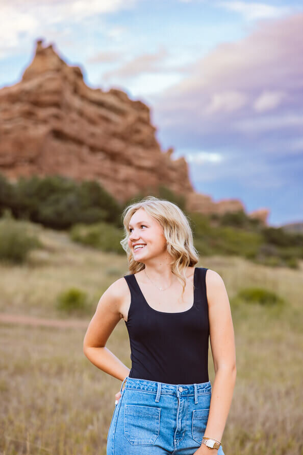 Girl looks over shoulder with mountains and sky behind her.