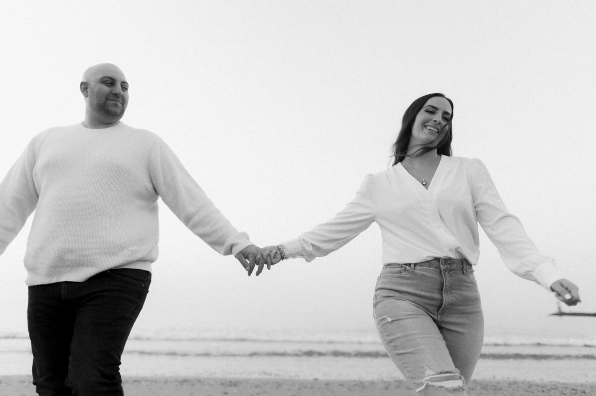 black and white photo of couple holding hands walking on the beach
