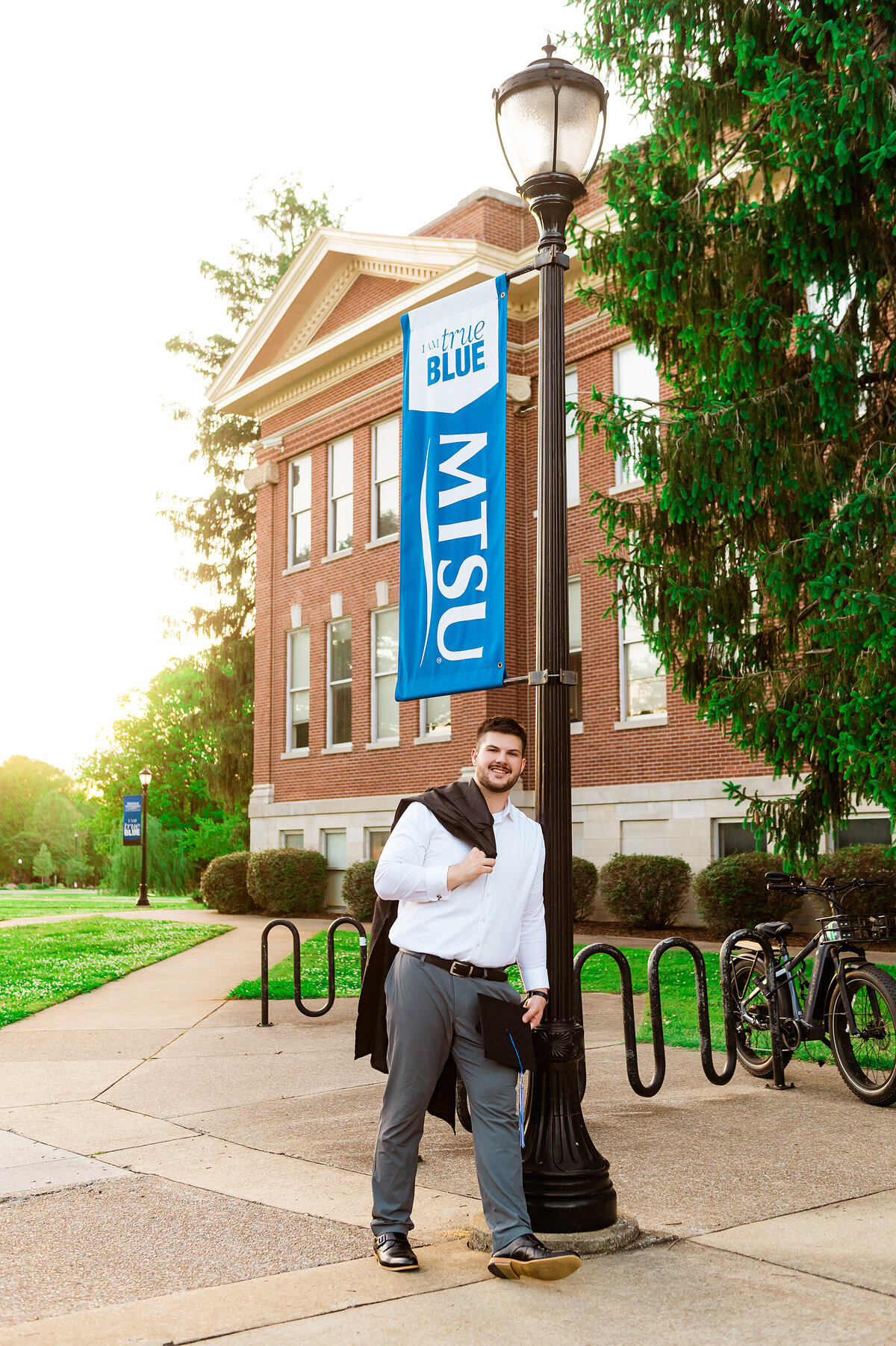 Senior holding his cap and gown in front of MTSU sign