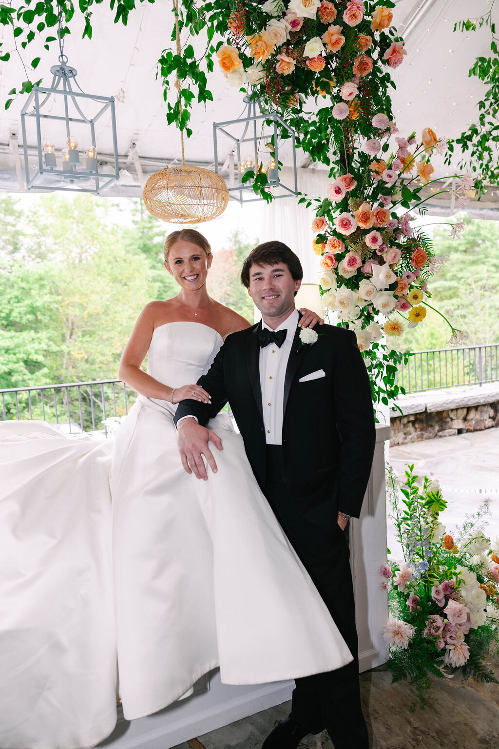Bride and groom posing beneath a colorful floral installation at their Bascom wedding in Highlands, North Carolina.