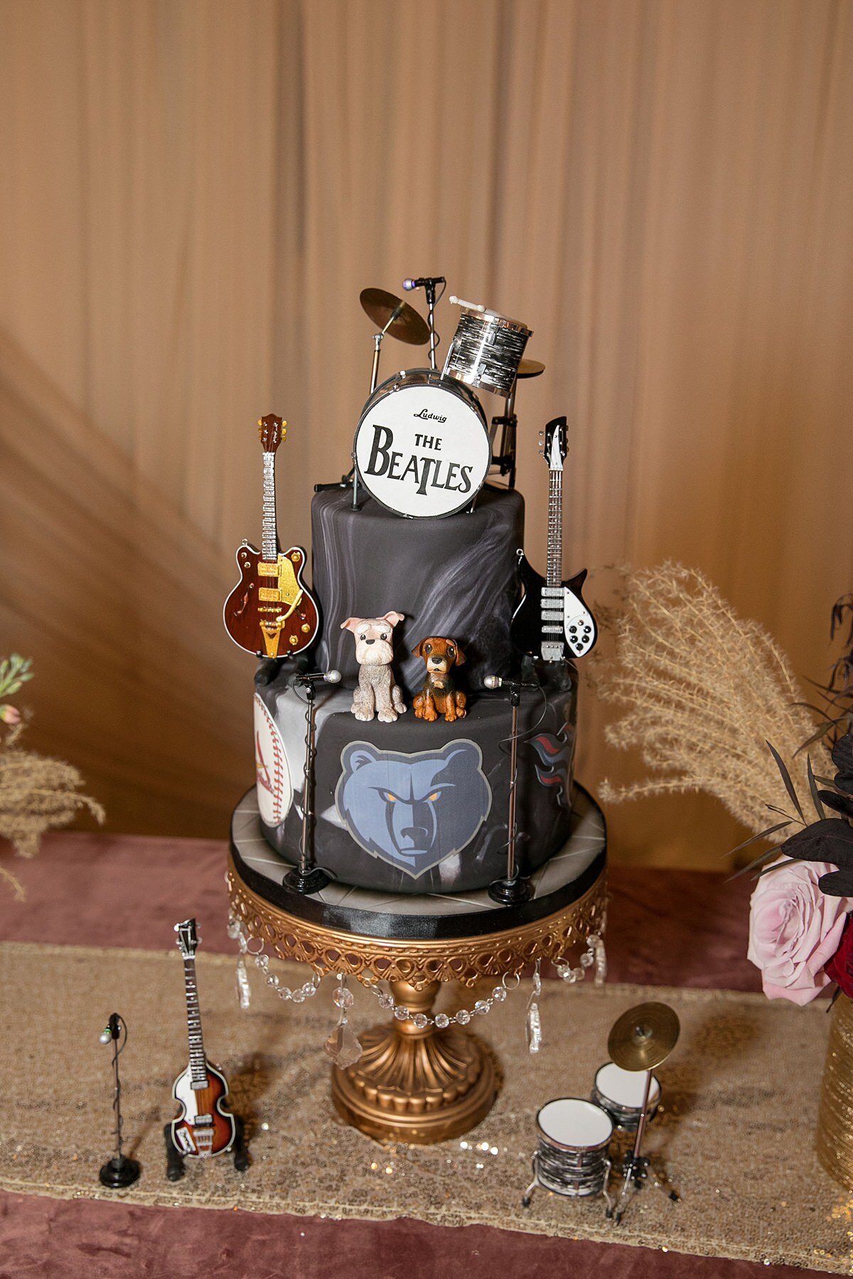 Two tier grooms cake with the Memphis grizzlies logo and a black and gray marbled fondant decorated with two small dogs and the Beatles drum kit cake topper, electric guitars and microphones.