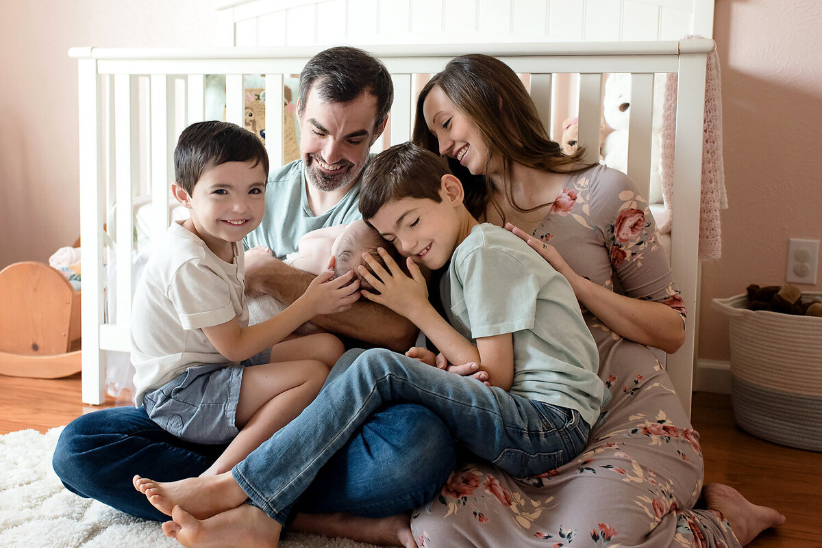 A family snuggling a brand new baby girl while sitting in front of the crib in her nursery in Richardson, TX.