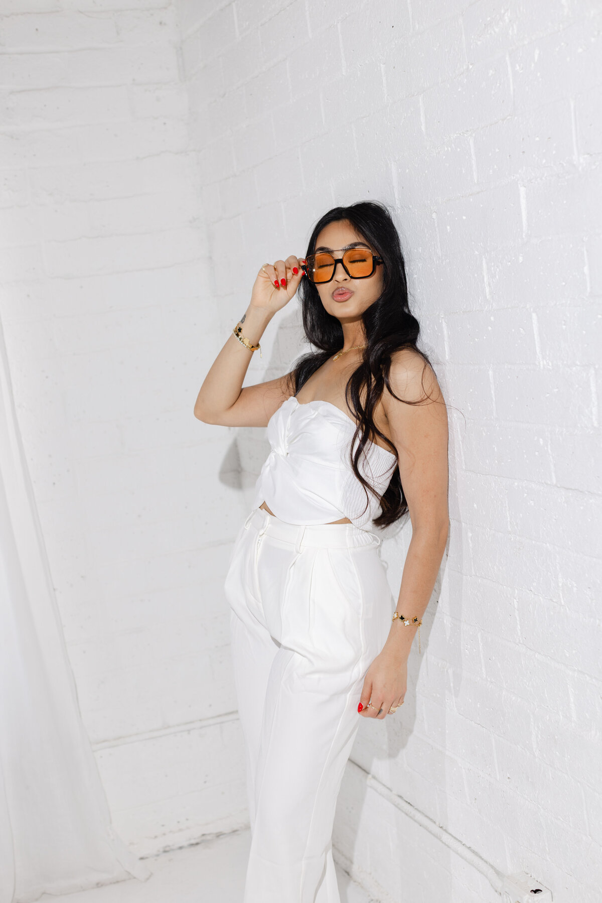 A sleek branding portrait featuring a woman in an all-white outfit with bold orange sunglasses. Crisp lighting and a white brick backdrop give this image a clean, high-fashion vibe. Photographed by Dani Lacey in Greenville SC