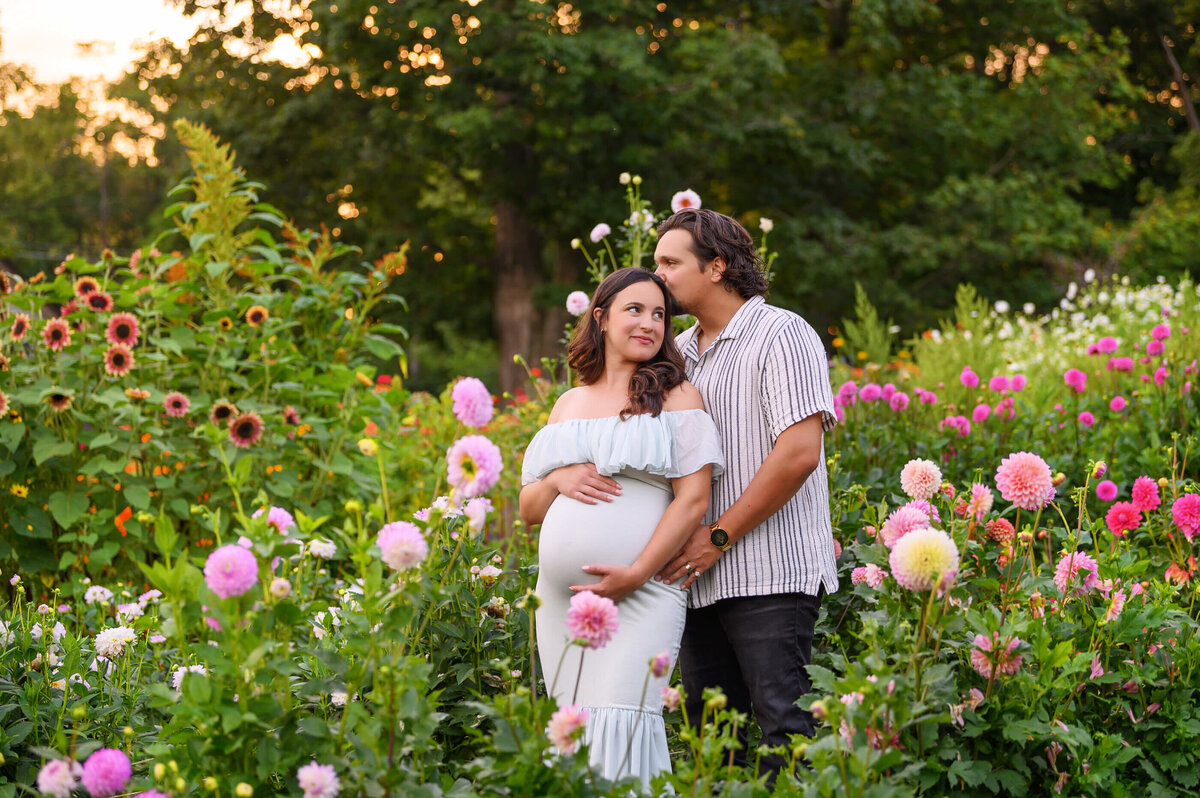 husband and wife cuddling outdoors for their maternity photography session at the flower farm in Burlington