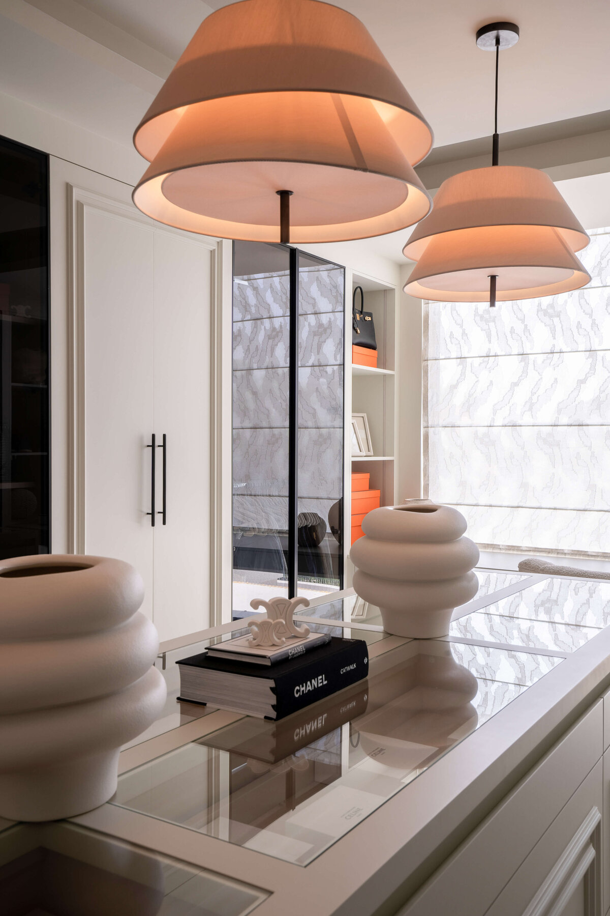 Closet island storage with glass display top. Above the cabinet are two chic light fixtures.