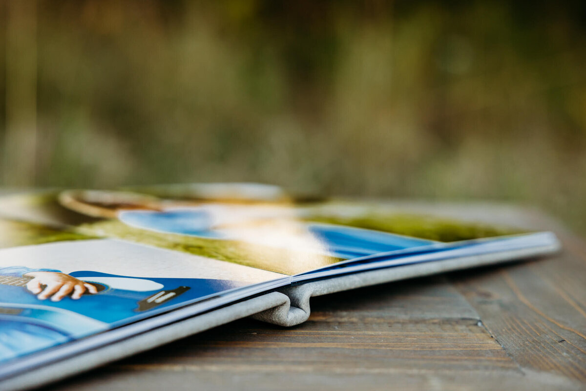 grey photo album opened to two images of a girl in a blue dress holding a blue guitar laying on a wood table captured by Ashley Kalbus